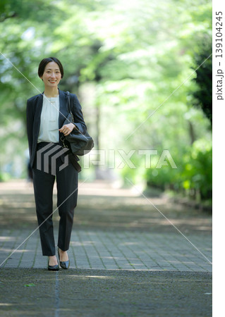 新緑の公園をビジネスバッグを持って歩く女性の営業マンの全身ポートレート仕事イメージ　コピースペース 139104245