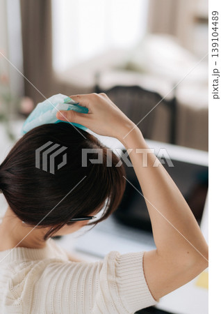 Exhausted asian woman feeling deeply stressed holds cold pack to relieve painful headache while using modern technology for daily work and difficult study at comfortable home desk Exhausted asian woman feeling deeply stressed holds cold pack to relieve painful headache while using modern technology for daily work and difficult study at comfortable home desk 139104489