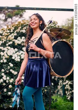 Beautiful dark-haired Latina woman posing with a drum and cymbals on her back, full of joy, a chinchinera, a street musician who dances and plays her drum in the streets. Chilean heritage 139104803
