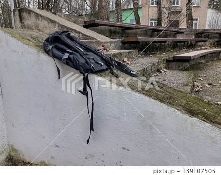 Black backpack resting on a white concrete wall Black backpack resting on a white concrete wall 139107505