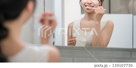 洗面所で鏡を見ながら歯磨きをする若いアジア人女性 洗面所で鏡を見ながら歯磨きをする若いアジア人女性 139107730