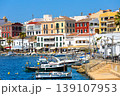 Boats are moored in the calm water in front of colorful houses in Mahon, Spain. 139107953