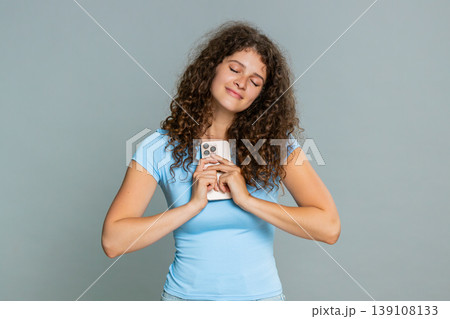 Woman joyfully reads lovely romantic message on smartphone pressing mobile phone close to heart Woman joyfully reads lovely romantic message on smartphone pressing mobile phone close to heart 139108133