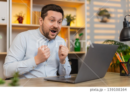 Young man on home table staring at laptop in shock with open mouth after astonishing breaking news Young man on home table staring at laptop in shock with open mouth after astonishing breaking news 139108164
