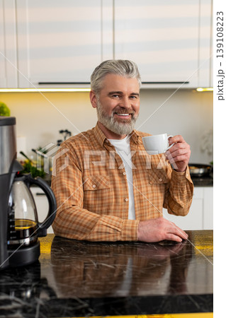 Middle-aged man pours fresh coffee from machine in kitchen enjoying morning routine energy at home 139108223