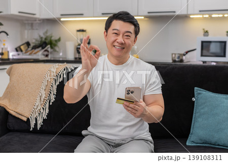 Asian man completes payment with smartphone and credit card smiles at confirmation shows thumbs up 139108311