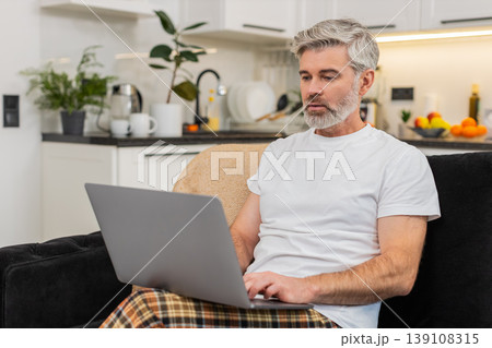 Middle-aged man with laptop on knees writes resume or works freelance remote work focused profile Middle-aged man with laptop on knees writes resume or works freelance remote work focused profile 139108315