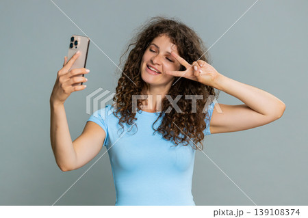 Young woman smiling carefree mood taking selfie photo on smartphone showing peace gesture hand sign 139108374