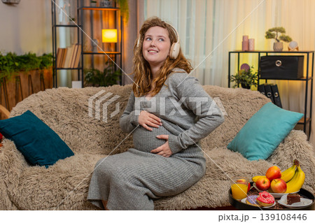 Pregnant young woman dancing with headphones, gently touching belly smiling positive mood and energy Pregnant young woman dancing with headphones, gently touching belly smiling positive mood and energy 139108446