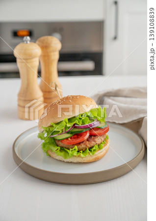 Beef burger with tomato, cheese, and lettuce on a plate on a light table with spice Beef burger with tomato, cheese, and lettuce on a plate on a light table with spice 139108839