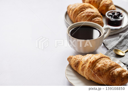 Cup of espresso coffee and fresh croissants on a light background with berry jam and spoon close up. 139108850