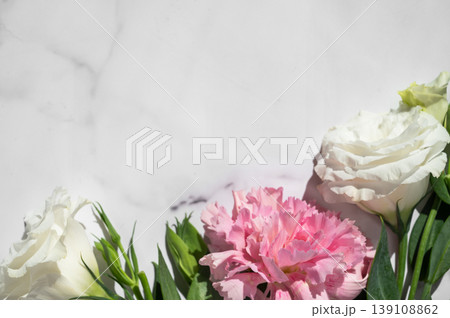 Fresh pink carnations and white eustomas on a marble background with sunlight, top view. Fresh pink carnations and white eustomas on a marble background with sunlight, top view. 139108862