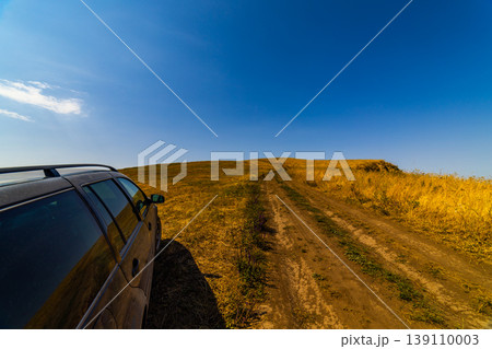 Dark gray station wagon parked on dirt road in rural landscape 139110003