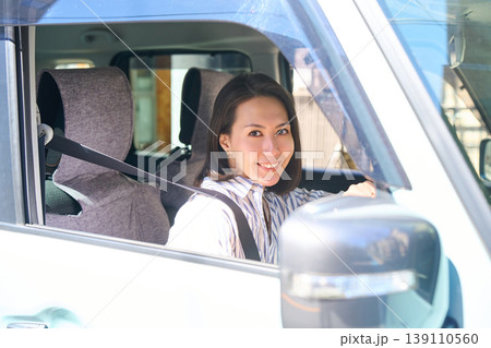 自動車の運転席でハンドルを握り、カメラ目線で微笑む日本人女性 139110560