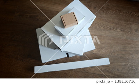 Stack of white boxes with a small brown box on top on wooden floor 139110716