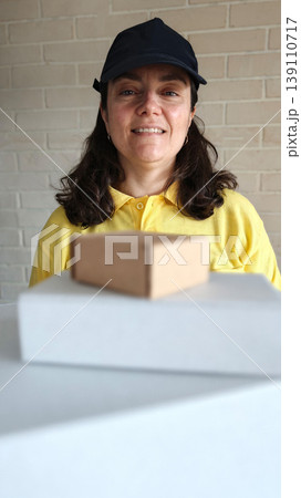 Woman stands in front of boxes in a room with white brick walls and smiles Woman stands in front of boxes in a room with white brick walls and smiles 139110717