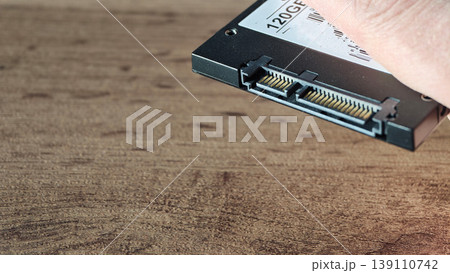 Close view of a hand holding a solid state drive above a wooden table Close view of a hand holding a solid state drive above a wooden table 139110742
