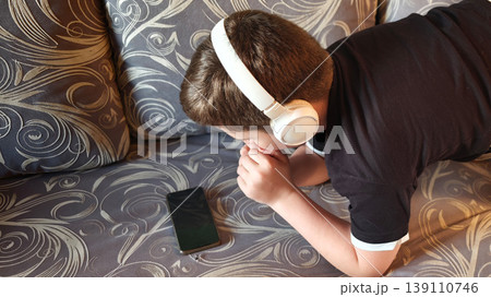 Child listens to music on smartphone while lying on couch during daytime 139110746