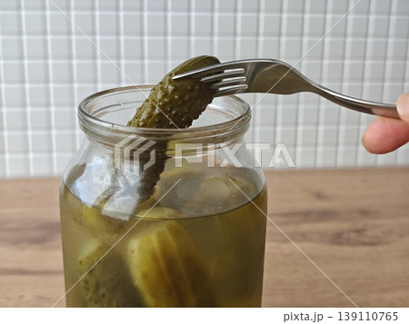 Person uses a fork to pick a pickle from a jar of pickled cucumbers Person uses a fork to pick a pickle from a jar of pickled cucumbers 139110765