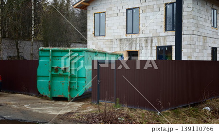 Construction site with a green dumpster near a building and a fence Construction site with a green dumpster near a building and a fence 139110766