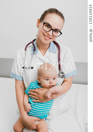 Positive pediatrician holding a baby, she sitting with child on a hospital bed. Care about infant health Positive pediatrician holding a baby, she sitting with child on a hospital bed. Care about infant health 139110914