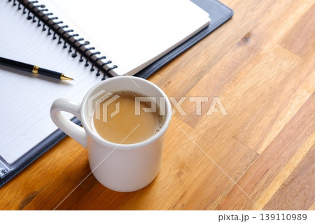 ミルクをたっぷり入れたコーヒー、カフェ・ラッテを飲みながら、ノートを広げてデスクワーク中のイメージ ミルクをたっぷり入れたコーヒー、カフェ・ラッテを飲みながら、ノートを広げてデスクワーク中のイメージ 139110989