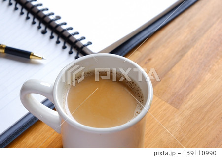 ミルクをたっぷり入れたコーヒー、カフェ・ラッテを飲みながら、ノートを広げてデスクワーク中のイメージ 139110990