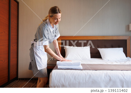 Housekeeper carefully arranging folded towels on hotel bed in guest room Housekeeper carefully arranging folded towels on hotel bed in guest room 139111402