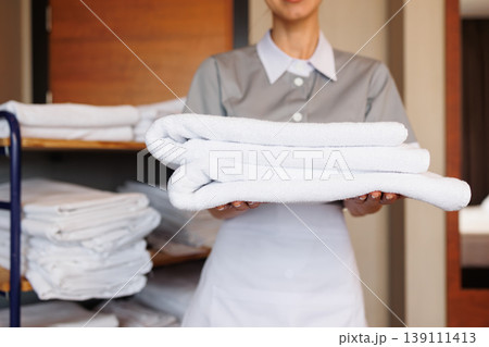 Hotel housekeeper presenting stack of fresh folded white towels in guest room Hotel housekeeper presenting stack of fresh folded white towels in guest room 139111413