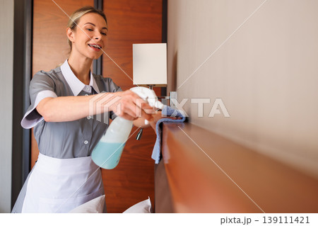 Professional hotel housekeeper cleaning wooden shelf with spray bottle in modern guest room Professional hotel housekeeper cleaning wooden shelf with spray bottle in modern guest room 139111421
