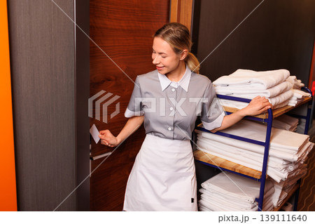 Hotel housekeeper opening guest room door with key card while standing beside fully loaded linen cart Hotel housekeeper opening guest room door with key card while standing beside fully loaded linen cart 139111640