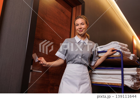 Housekeeping worker using key card at hotel room door with fresh linens on service cart Housekeeping worker using key card at hotel room door with fresh linens on service cart 139111644