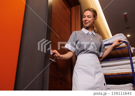 Low angle portrait of hotel maid opening room door beside housekeeping cart with clean laundry Low angle portrait of hotel maid opening room door beside housekeeping cart with clean laundry 139111645