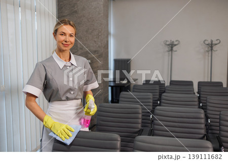 Professional janitor standing with cleaning supplies in office conference room 139111682