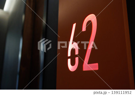Modern Hotel Corridor with Illuminated Room Number 62 Sign on Dark Wooden Wall Modern Hotel Corridor with Illuminated Room Number 62 Sign on Dark Wooden Wall 139111952