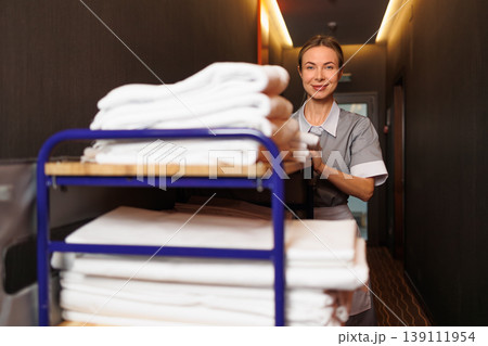 Smiling Hotel Maid with Laundry Trolley Full of Clean Towels in Hallway 139111954