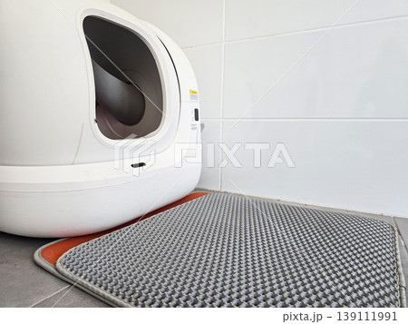 Modern automatic self-cleaning cat litter box placed on a tiled floor with a mat. Concepts of pet care technology, home convenience, and smart living solutions. Modern automatic self-cleaning cat litter box placed on a tiled floor with a mat. Concepts of pet care technology, home convenience, and smart living solutions. 139111991