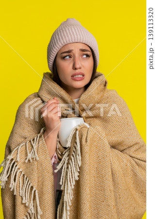 Woman wrapped in blanket wearing hat adding honey to tea slowly drinking caring for sore throat Woman wrapped in blanket wearing hat adding honey to tea slowly drinking caring for sore throat 139113320