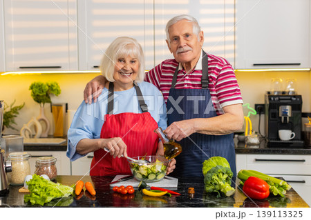 Senior old woman man smiling pouring dressing on fresh salad in home kitchen for diet wellness plan Senior old woman man smiling pouring dressing on fresh salad in home kitchen for diet wellness plan 139113325