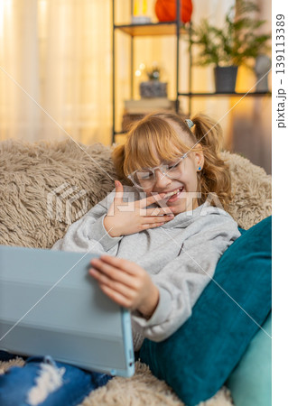 Young teenager girl enjoys watching online cartoons on tablet screen at home, giggling laughing 139113389