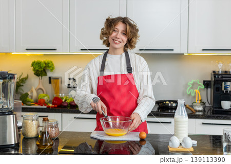 Young woman whisking eggs in kitchen while preparing healthy breakfast meal for home cooking routine 139113390