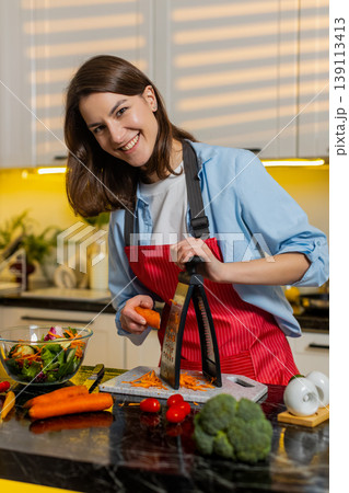 Young woman grating carrot into fresh salad in modern home kitchen for healthy diet meal prep daily Young woman grating carrot into fresh salad in modern home kitchen for healthy diet meal prep daily 139113413