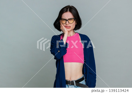 Woman touching cheek grimacing in pain clearly showing severe toothache discomfort dental problem Woman touching cheek grimacing in pain clearly showing severe toothache discomfort dental problem 139113424