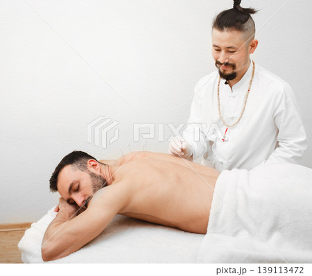 Reflexologist doing an acupuncture procedure for man with pain in his back. Acupuncture treatment of the back. Painless procedure Reflexologist doing an acupuncture procedure for man with pain in his back. Acupuncture treatment of the back. Painless procedure 139113472