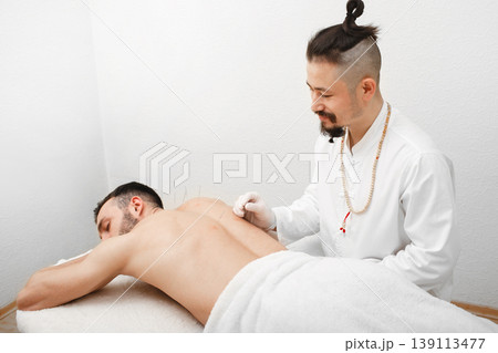 Reflexologist doing acupuncture to treat male patient. Acupuncture is part of traditional Chinese medicine 139113477