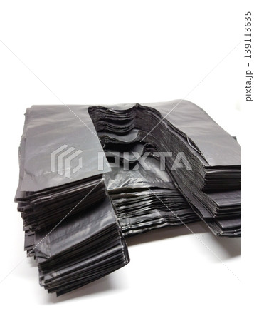 Isolated close-up view of a large, folded stack of bulk black plastic t-shirt handle bags. 139113635