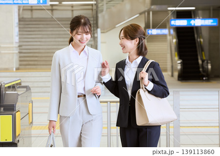 駅の改札付近で笑顔で会話しながら歩く二人の若い女性ビジネスパーソン・スーツ姿の通勤風景 駅の改札付近で笑顔で会話しながら歩く二人の若い女性ビジネスパーソン・スーツ姿の通勤風景 139113860