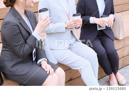 屋外のベンチでコーヒーを持ちながら談笑する3人のスーツ姿の女性ビジネスパーソン・休憩時間の会話 屋外のベンチでコーヒーを持ちながら談笑する3人のスーツ姿の女性ビジネスパーソン・休憩時間の会話 139113880
