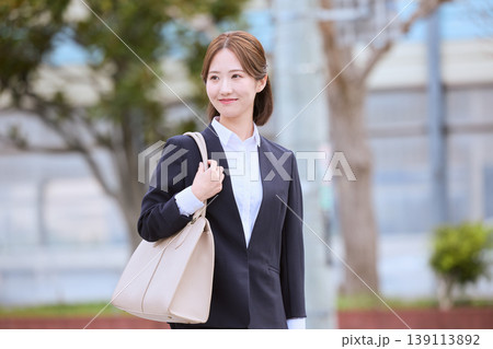 春の街中を歩くリクルートスーツ姿の若い女性・就職活動中の女子大学生が笑顔で通勤するイメージ 春の街中を歩くリクルートスーツ姿の若い女性・就職活動中の女子大学生が笑顔で通勤するイメージ 139113892