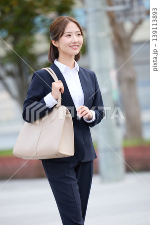 ビジネスバッグを持って笑顔で歩くリクルートスーツ姿の若い女性・就職活動中の女子大学生 ビジネスバッグを持って笑顔で歩くリクルートスーツ姿の若い女性・就職活動中の女子大学生 139113893